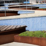 En blomlåda och en sitt bänk av trä framför en blå vägg. En grå gång bakom i sicksackmönster.