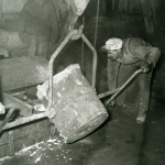 En man med keps böjer sig ner för att välta ut innehållet i en stor behållare.