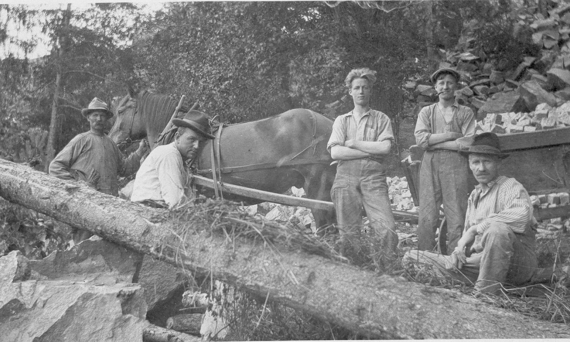 Fem män och en häst som drar en vagn med gatsten.