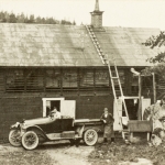 Två män och en gammal bil framför en lada.