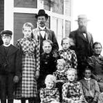 Ett svartvitt foto av barn och vuxna uppställda framför ett hus.