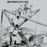 Svartvitt foto av elva pojkar i badbyxor som klättrar på en kran intill vattnet.