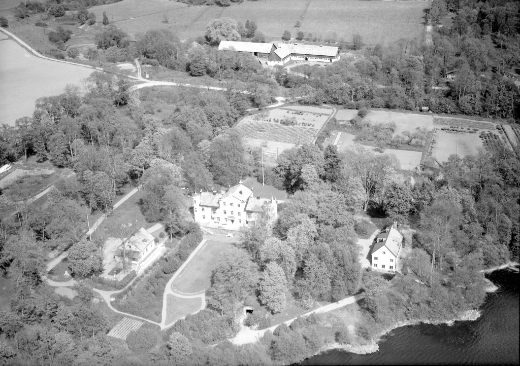 Flygfoto över en gård tornprydd gård med flygelbyggnader och park. Två ekonomibyggnader, lada eller stall syns också.