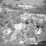 Flygfoto över en gård tornprydd gård med flygelbyggnader och park. Två ekonomibyggnader, lada eller stall syns också.