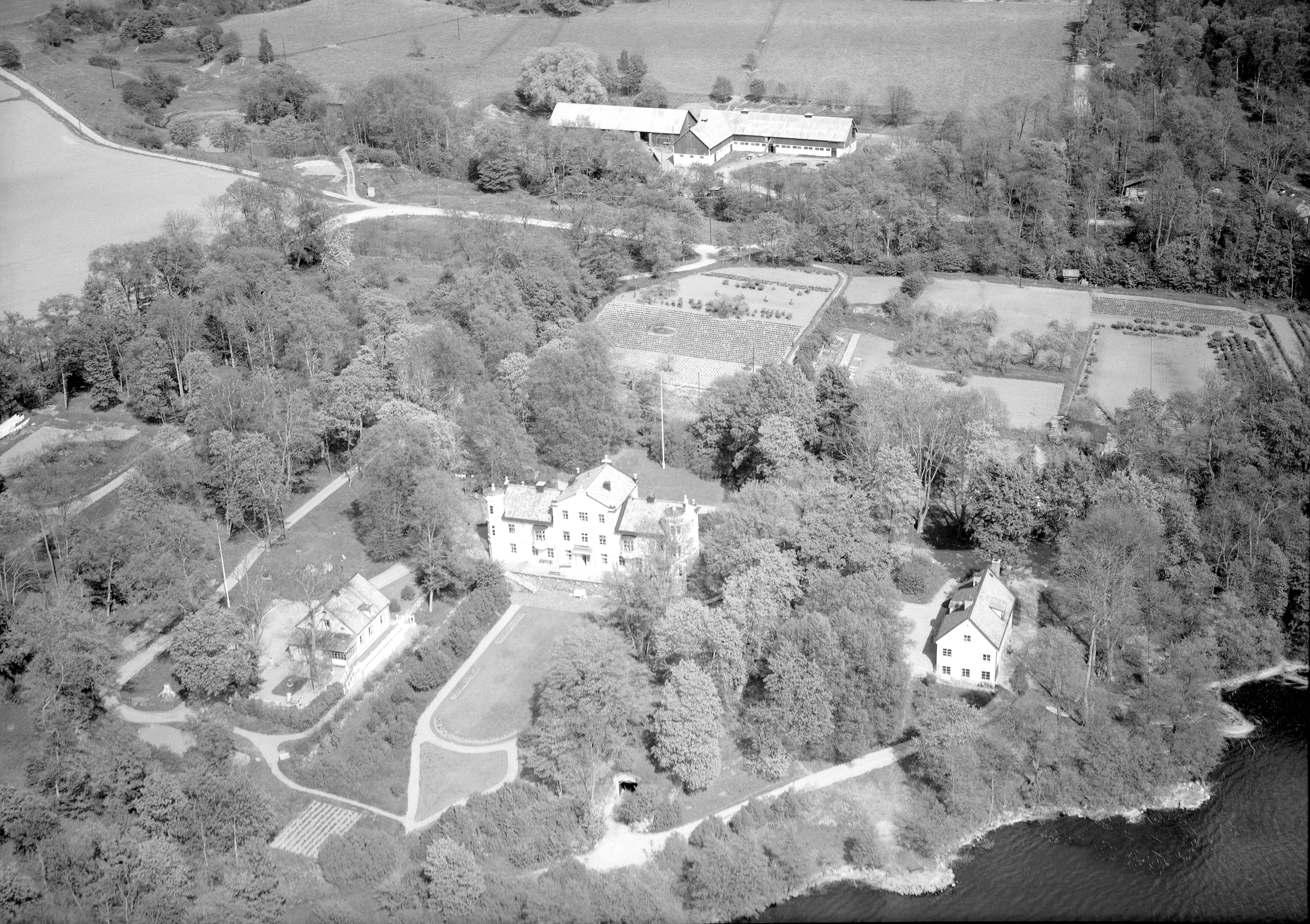 Flygfoto över en gård tornprydd gård med flygelbyggnader och park. Två ekonomibyggnader, lada eller stall syns också.