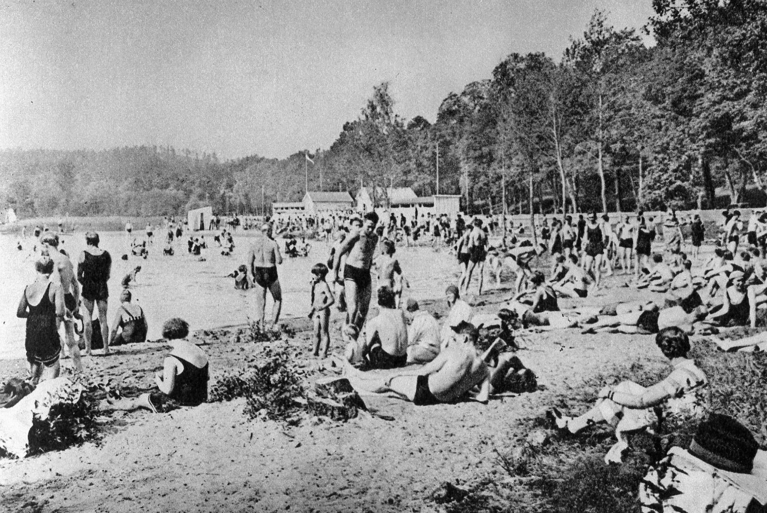 Svartivtt foto av ett hundratal människor på en sandstrand.