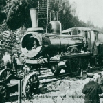 En svartvit bild av människor på och runt spåret där ett trasigt ånglok står.