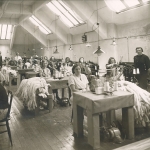 Kvinnor sitter vid symaskiner i ett stort rum med takfönster.