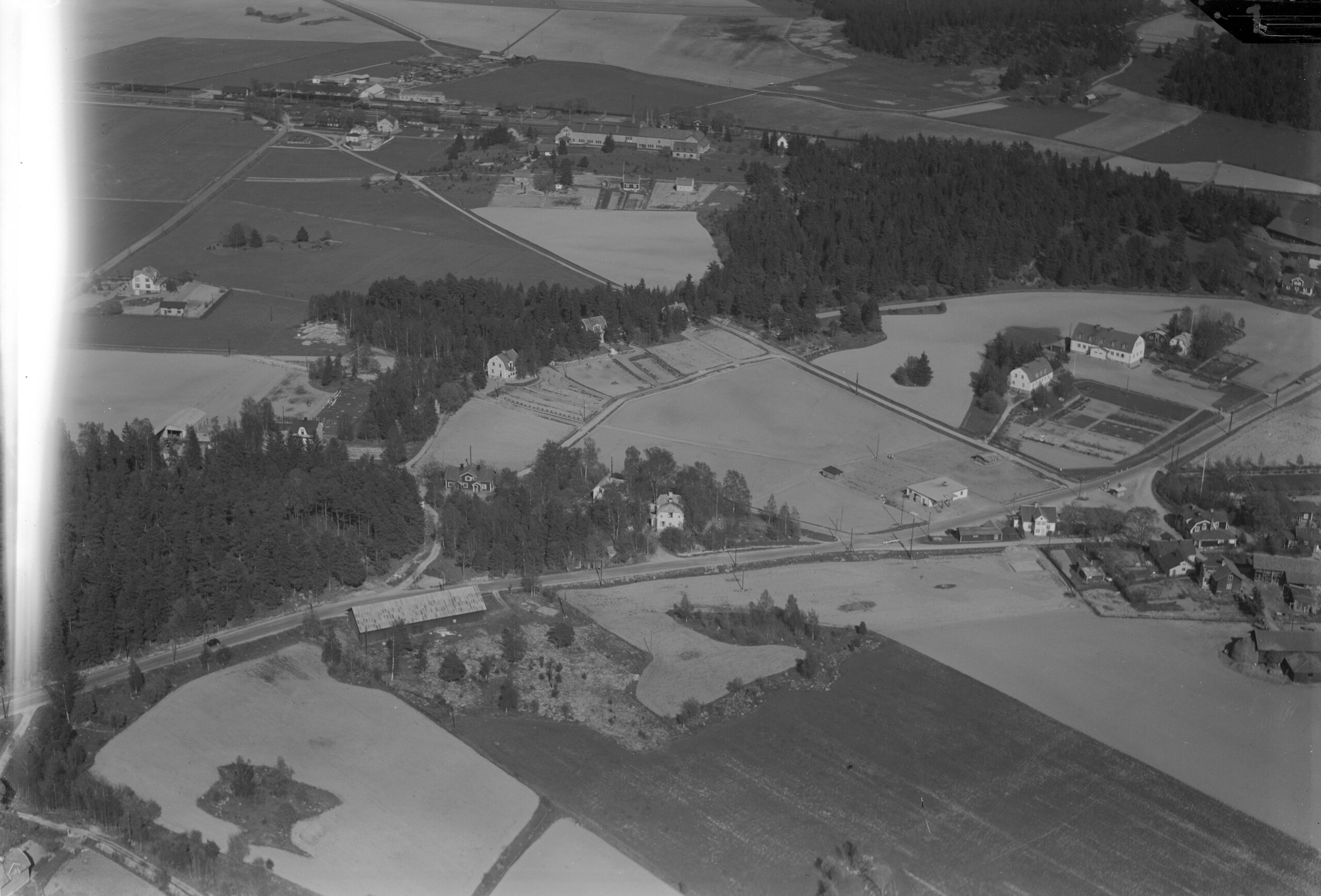 Ett svartvitt flygfoto med åkrar och några hus.