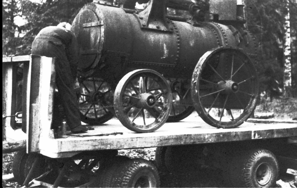 Lokomobilen står på ett lastbilsflak på detta svartvita foto.