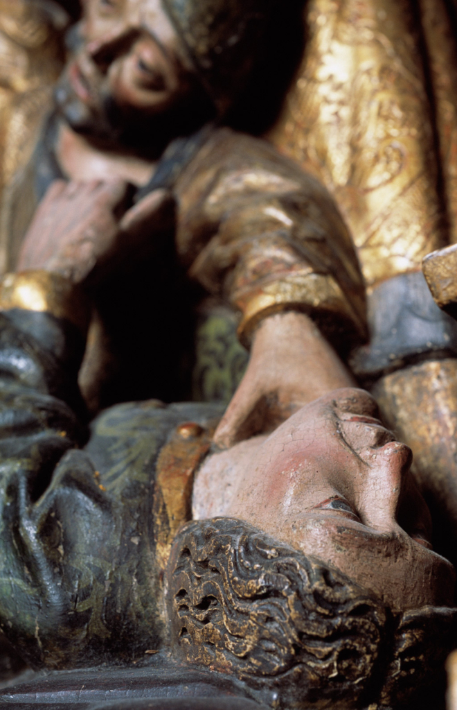 Snidad träfigur av en man som ligger ner med en hand mot strupen.