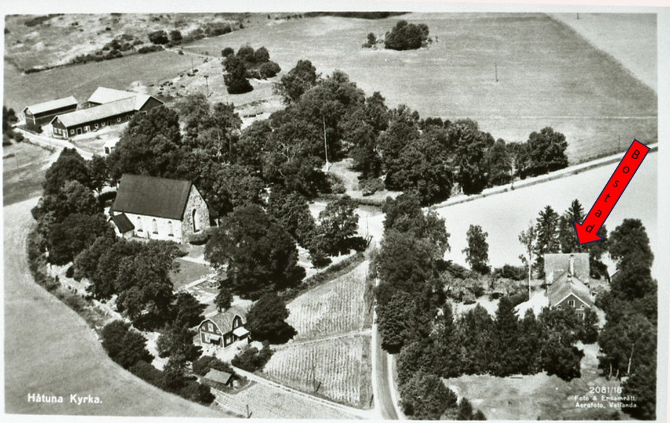 Ett svartvitt vykort över en kyrka med ett par hus i närheten, fotograferat från luften.