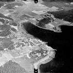 Svartvitt flygfoto där flyganläggningen byggnader strå ensamma vid vattnet.