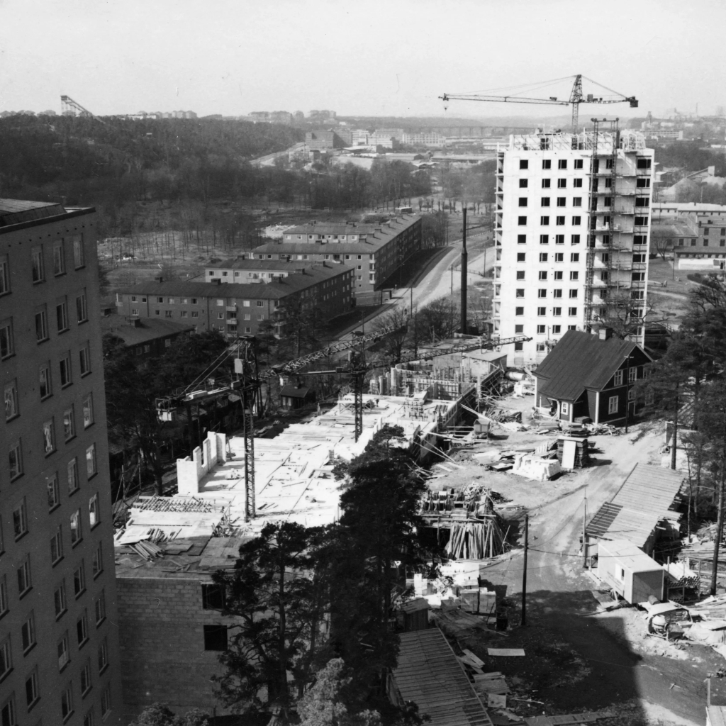 Foto taget från höghus. Bygge pågår men ett äldre rött trähus står kvar.