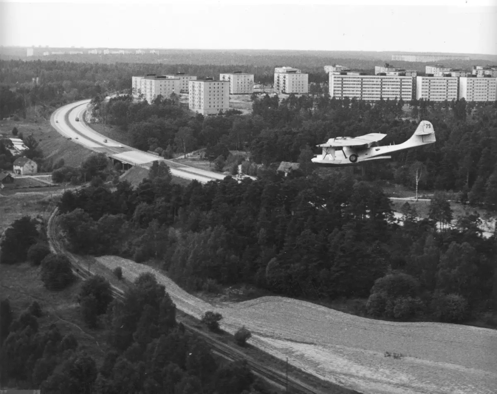 Planet flyger på låg höjd över Roslagsbanans spår, Norrtäljevägen och höghusen i Hägernäs.
