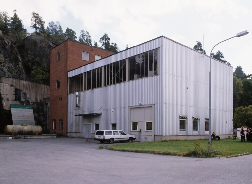 Industribyggnad i tegel och korrugerad plåt intill en bergsvägg.