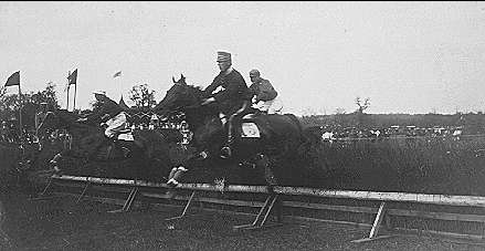 Svartvittt fotografi. Ryttare till häst hoppar över hinder.