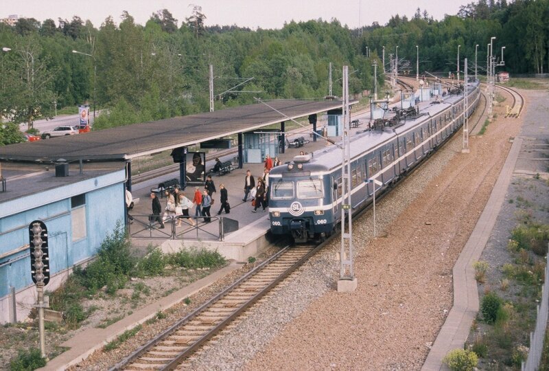 Ett tåg står på en perrong. På perrongen står flera människor.