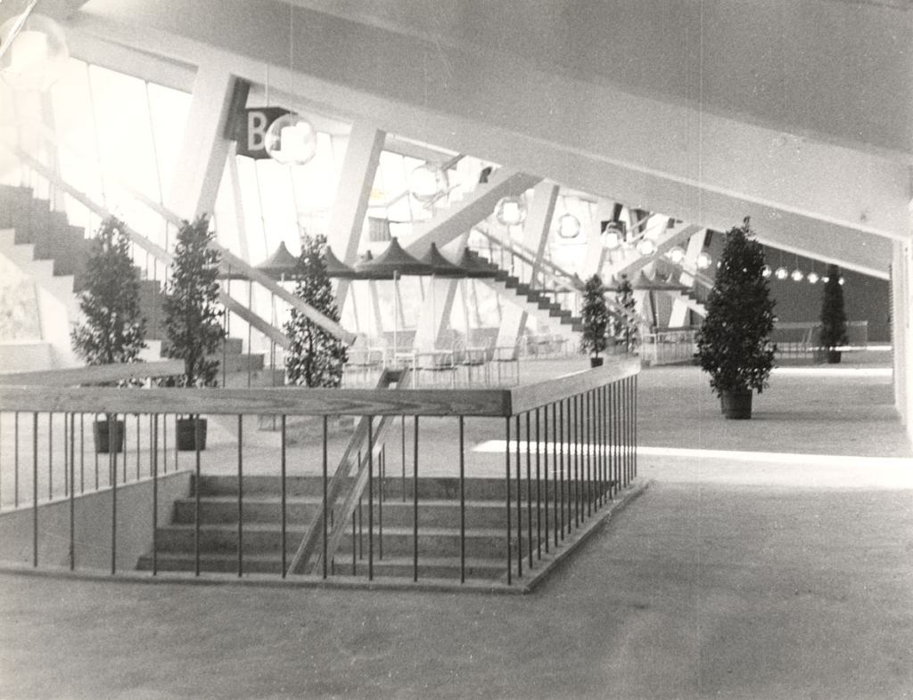 Svartvitt foto. Interiör av byggnad med stora fönster.