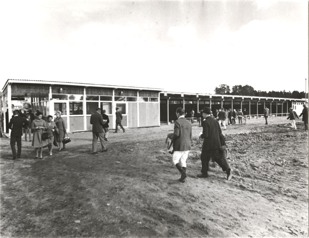 Svartvitt foto. Människor passerar genom biljettkassorna.