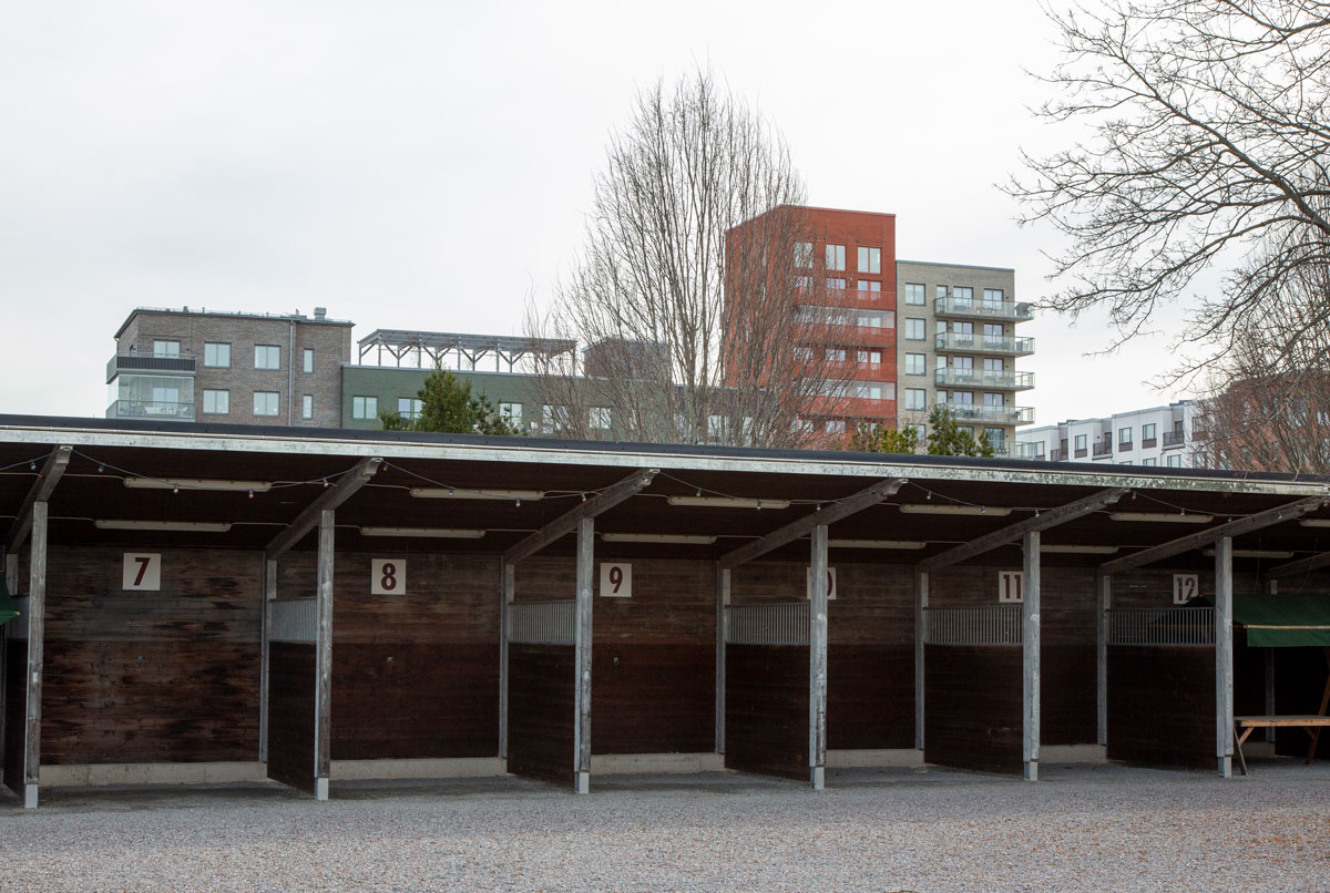 Foto. Låg byggnad i brunt tr. I bakgrunden står nybyggda lägenhetshus.