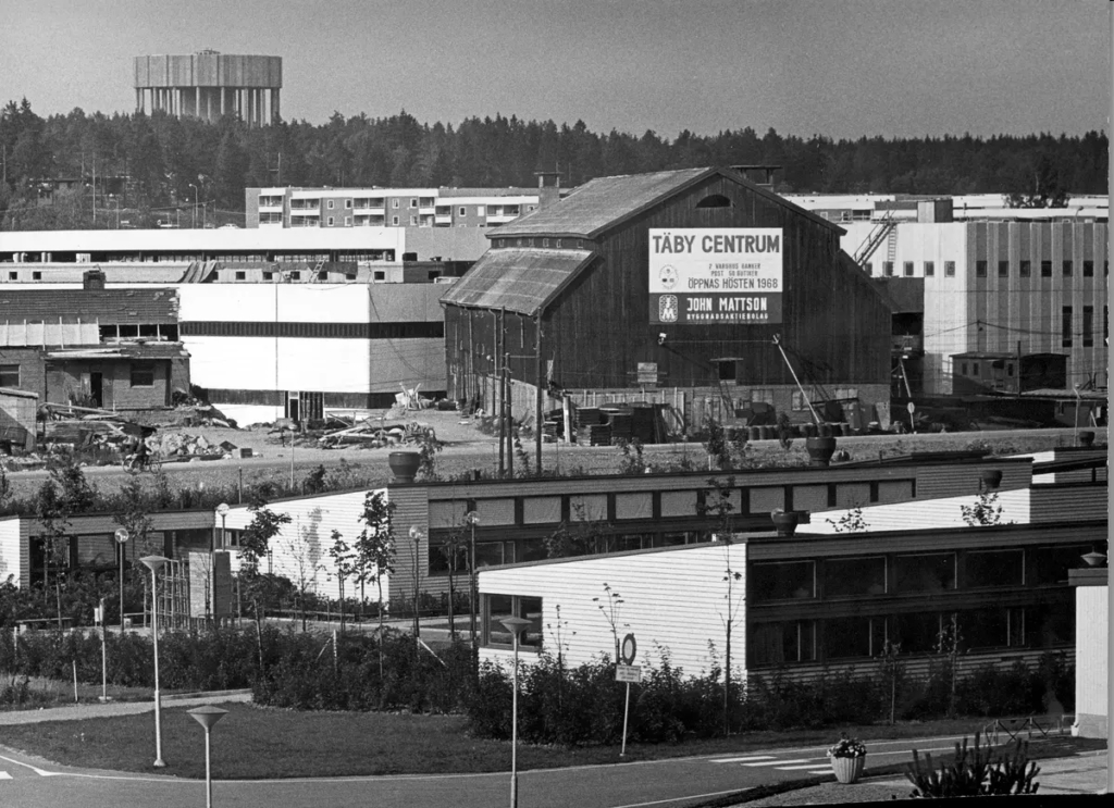 Svartvitt foto. En äldre lada med skylt som anger "Täby centrum".