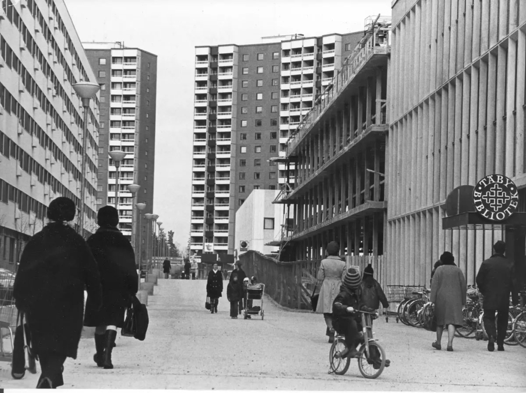 Svartvitt foto. Människor på gata i centrumbebyggelse.