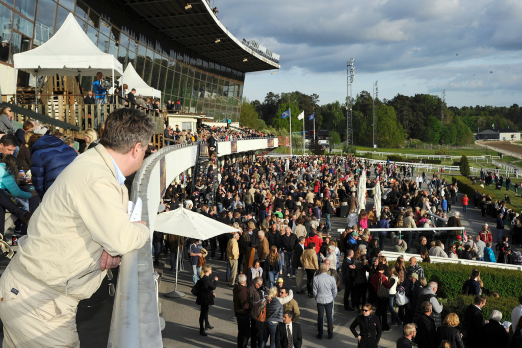 Folksamling. Läktarbyggnad i bakgrunden.