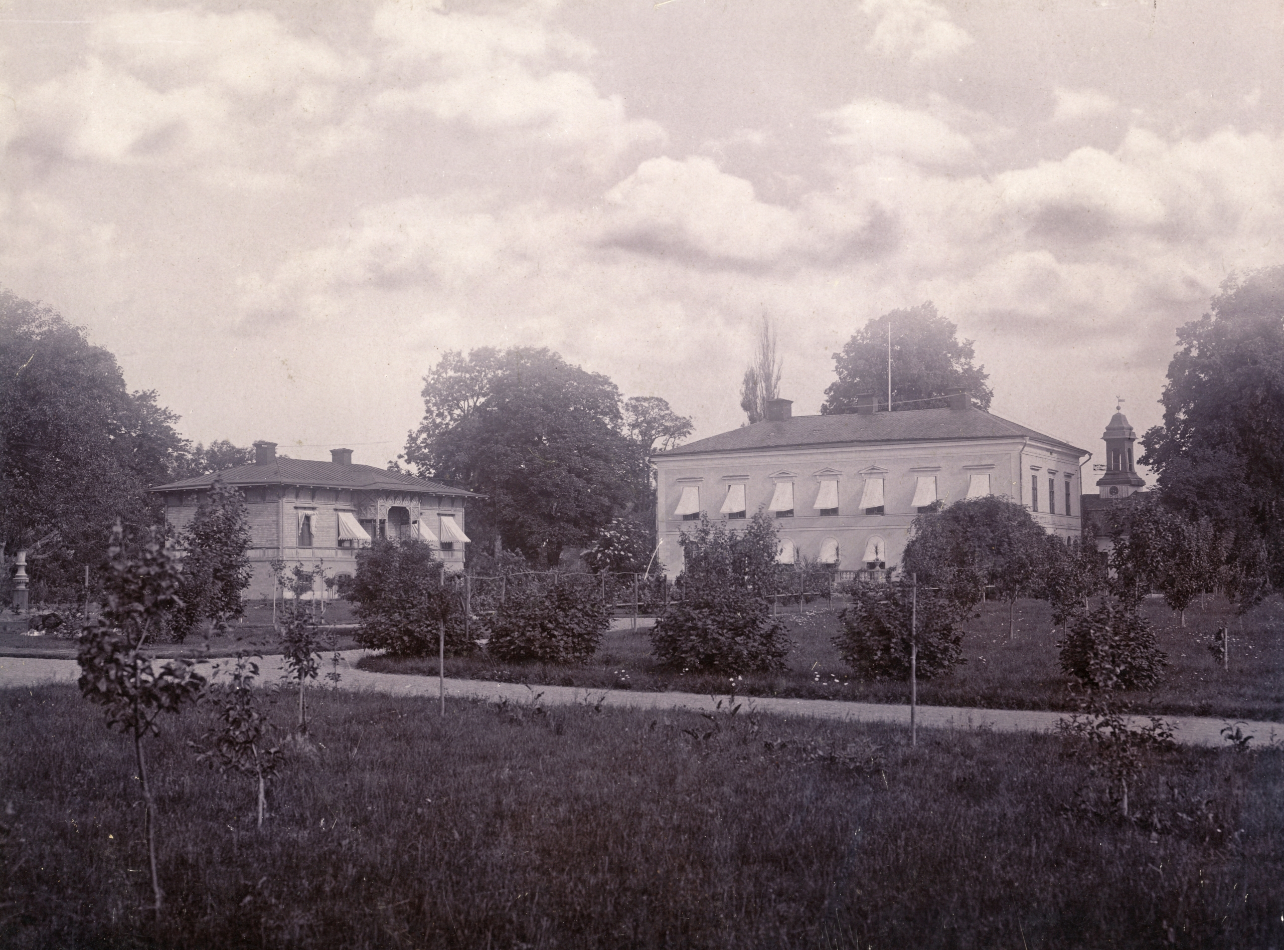Gårdens huvudbyggnad och en flygelbyggnad. Grönska och nyplanterade träd.