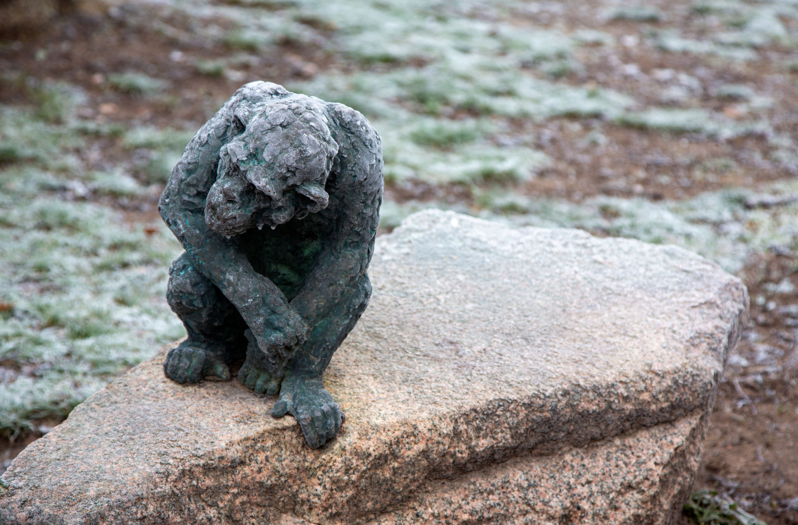 Skulptur av en apa av brons som sitter på en sten.
